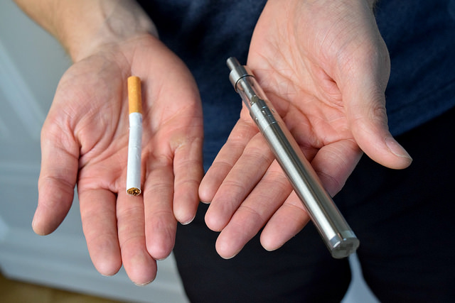 a man holding a cigarette in one hand and a vape in another