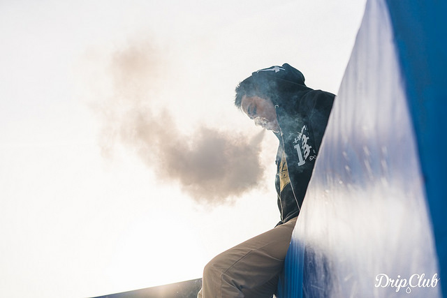 man with a black hoody sat on a wall vaping