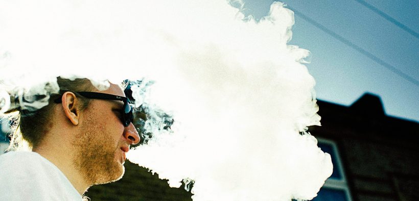 white man in sunglasses producing a cloud of vapour after using e-cigarette