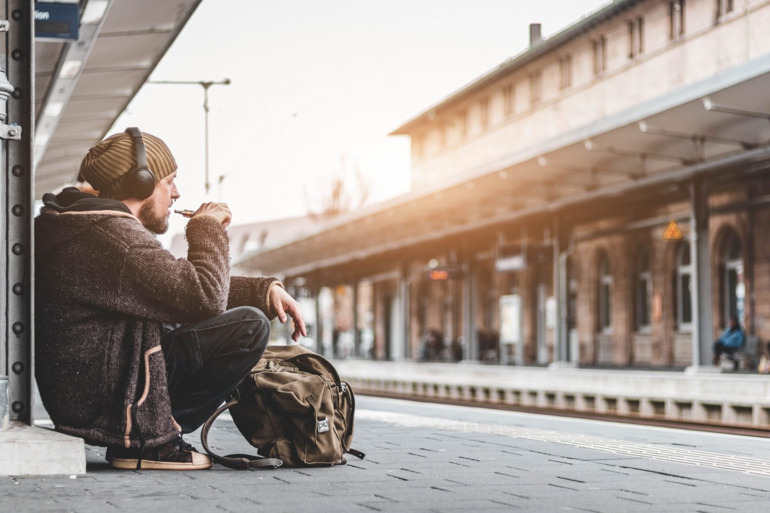 male vaper with headphones sat at a train station vaping