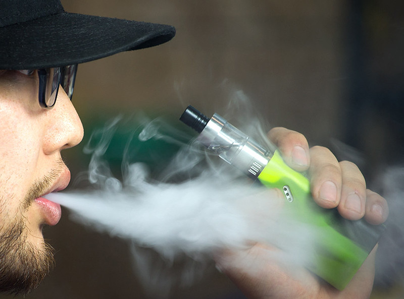 man vaping on a green mod and blowing up clouds