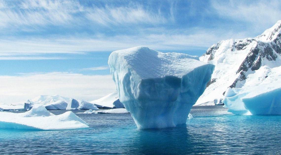 an iceberg appearing out of a deep blue sea surrounded by mountains of glaciers