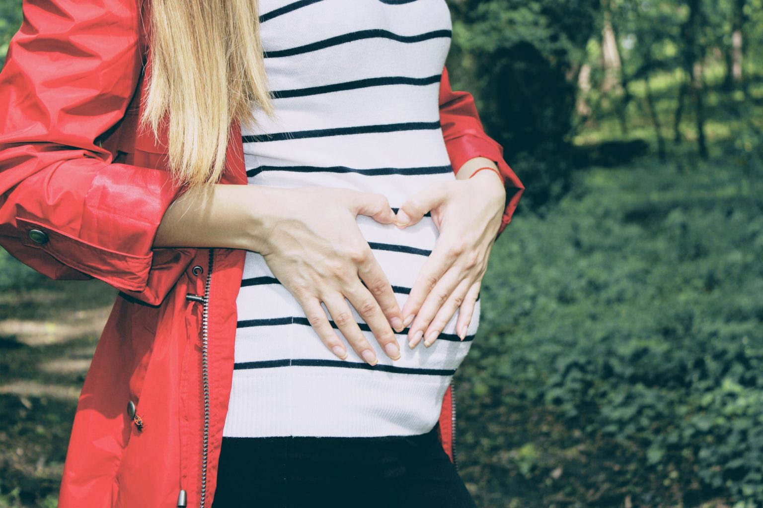 Blonde pregnant woman in a black and white jump with a red coat holding stomach