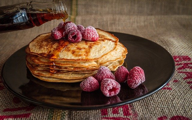 Pancakes drizzled in maple syrup topped with raspberries