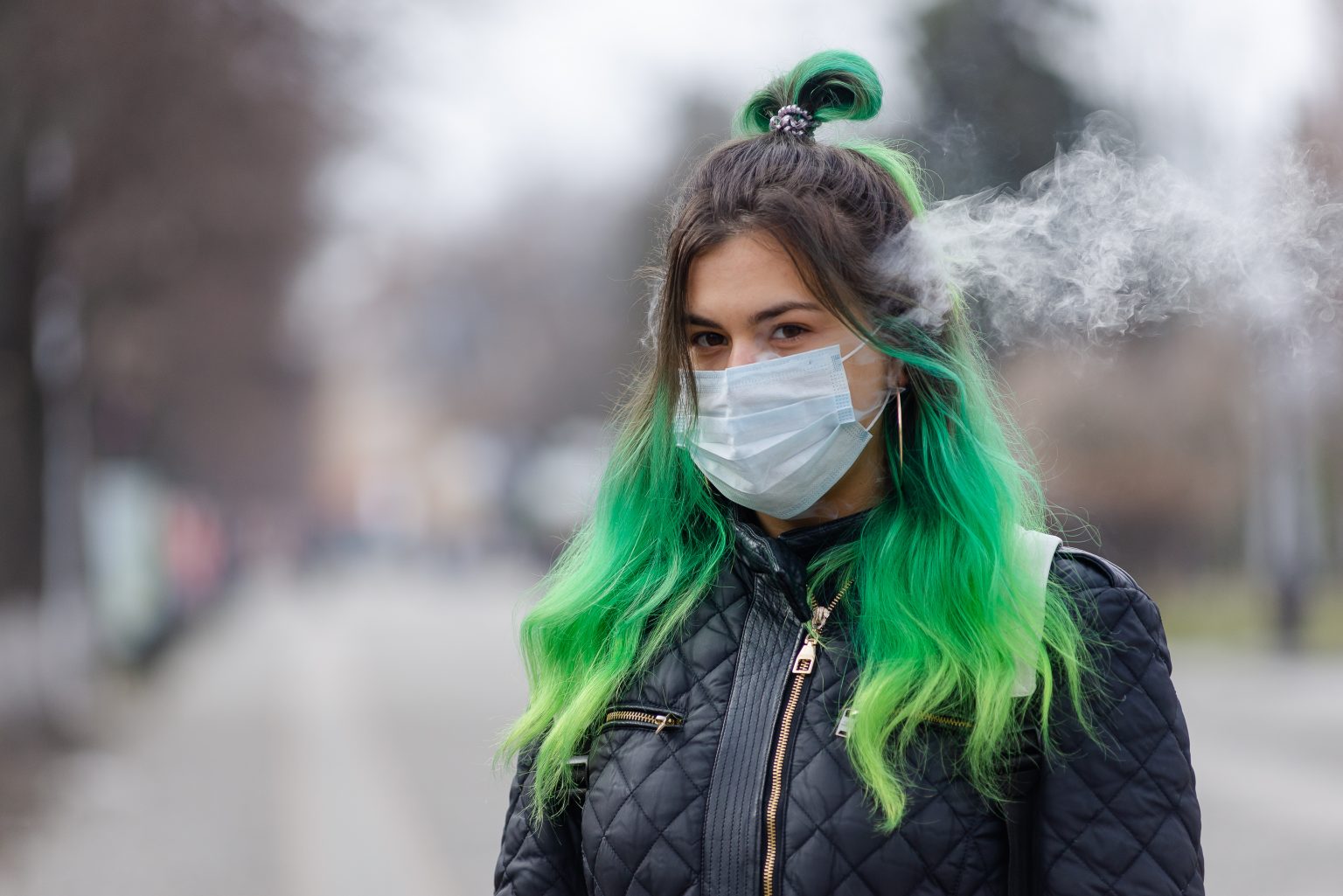 woman with green hair and a face mask vaping