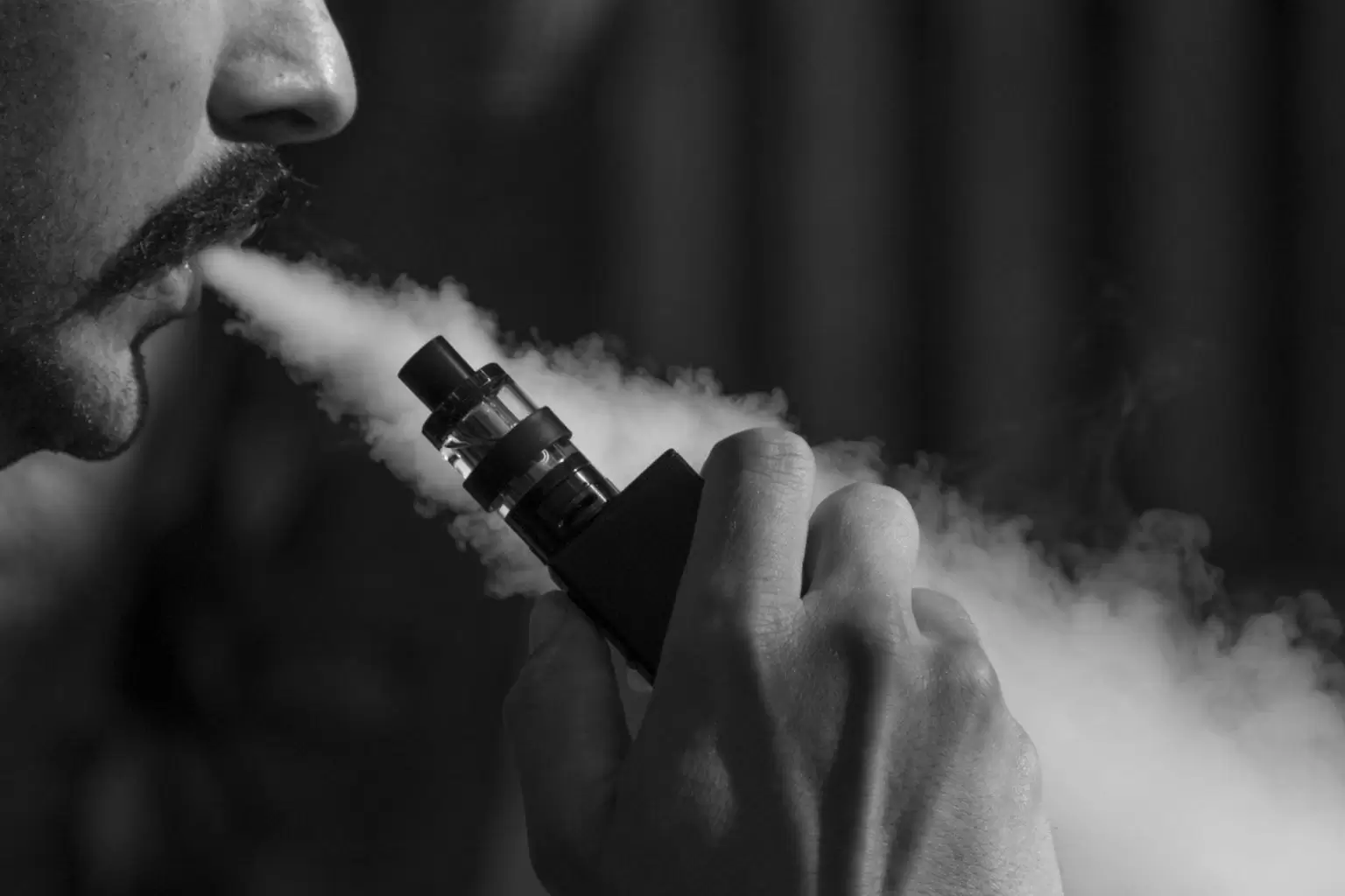 A black and white image of a man exhaling a vape device