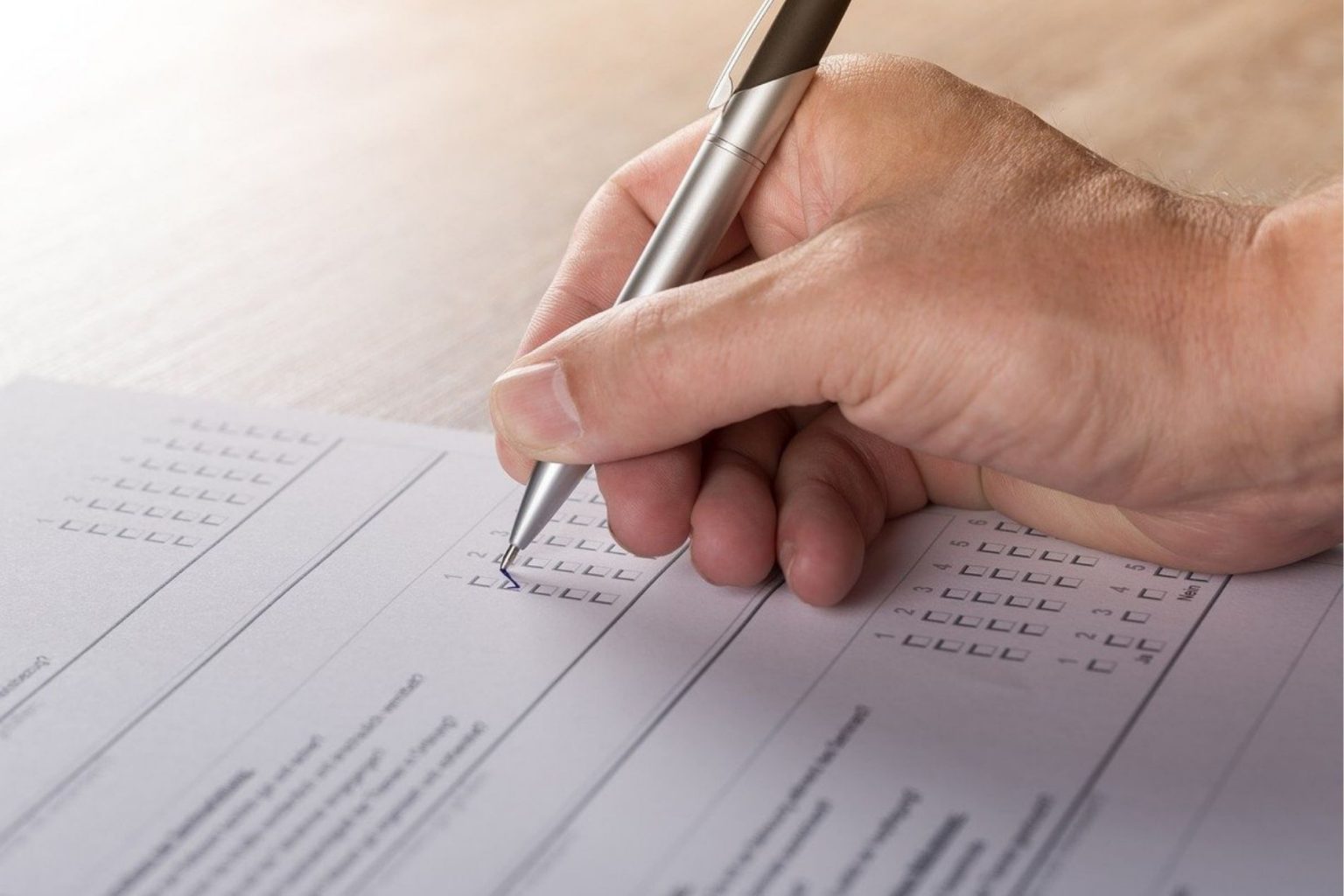 A white hand holding a pen to paper for a survey