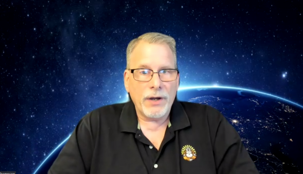 A man sits in front of a blue earth screen on Zoom