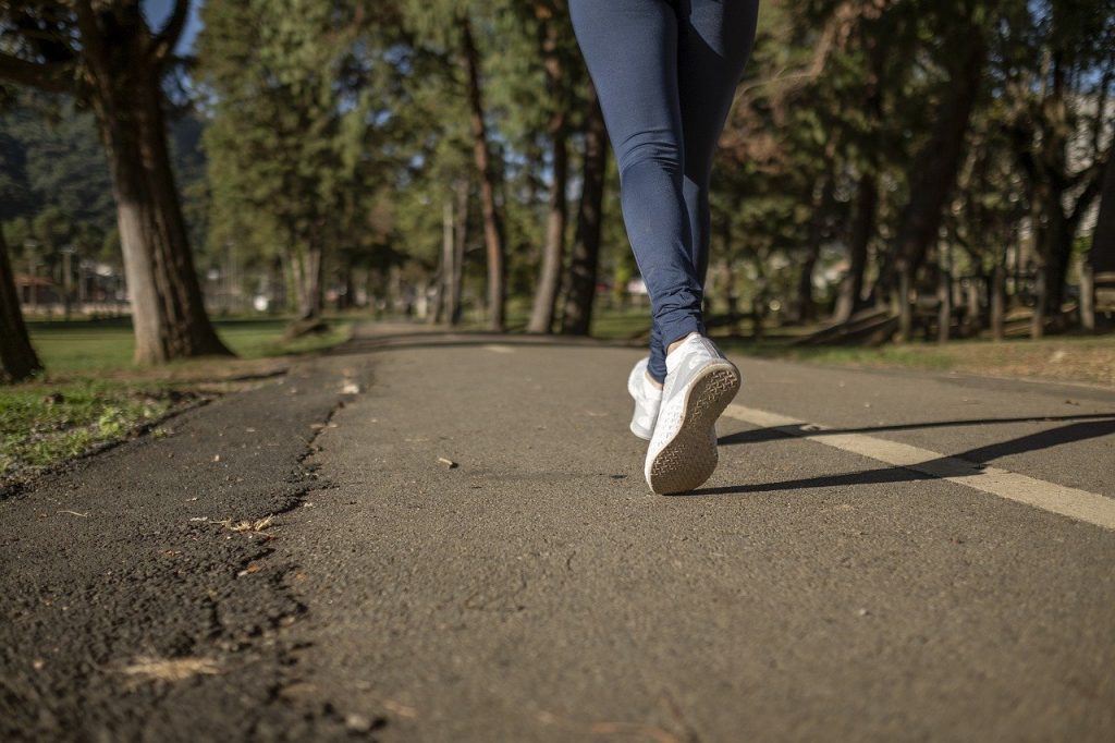 A countryside road with a person jogging in the middle wearing blue leggings and white sneakers