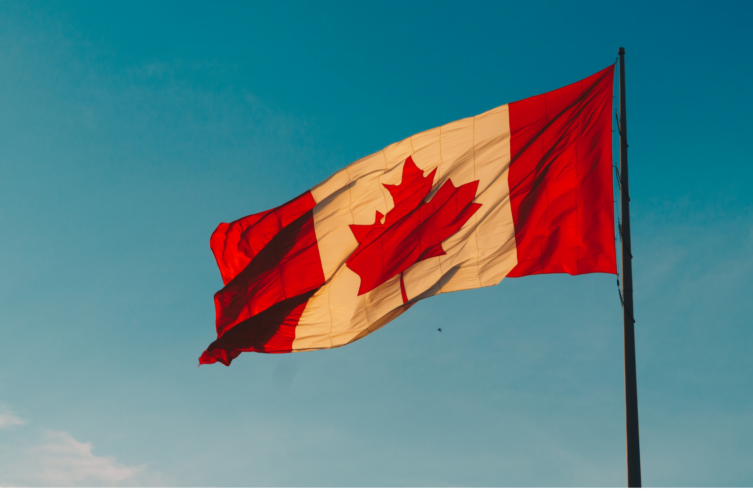 A Canadian flag on a bright blue sky