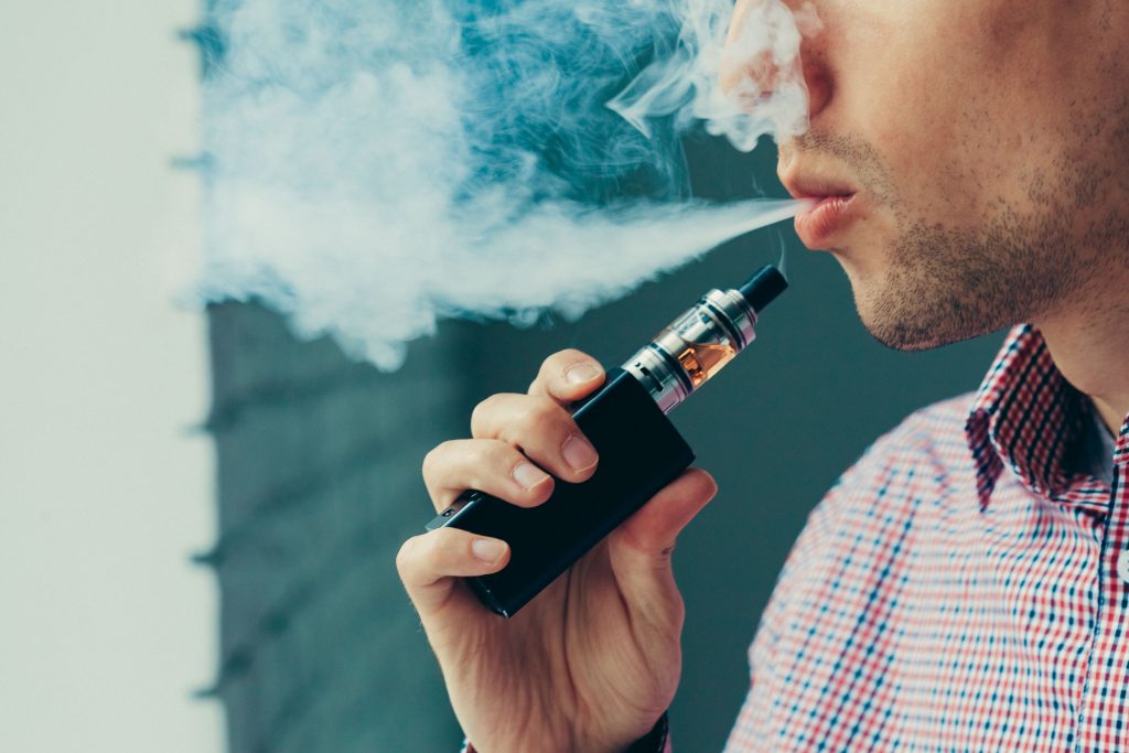 Man taking a puff on his vaping device and blowing vapour.