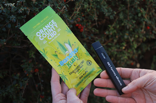 orange county cbd green banana kush plastic packaging and black disposable vape pen 