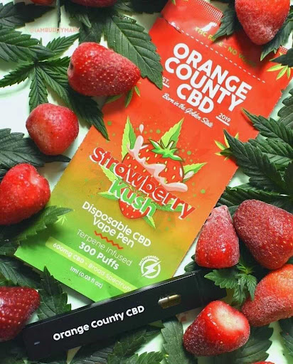 orange county cbd disposable vape pen packaging and disposable device surrounded by strawberrys from instagram account @iambuddymary