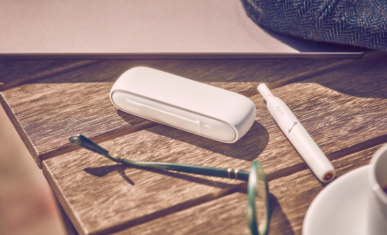 white iqos heated tobacco device and charging pod on a wooden bench