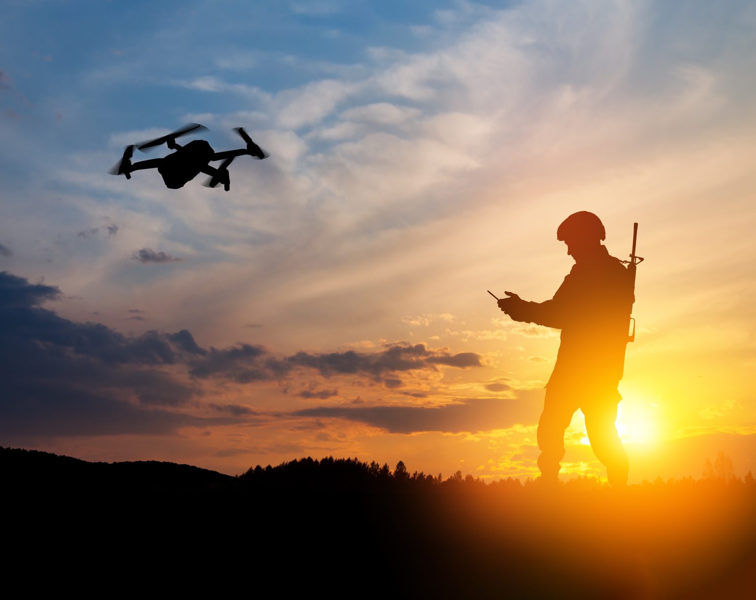 Silhouette of soldier are using drone and laptop computer for scouting during military operation against the backdrop of a sunset