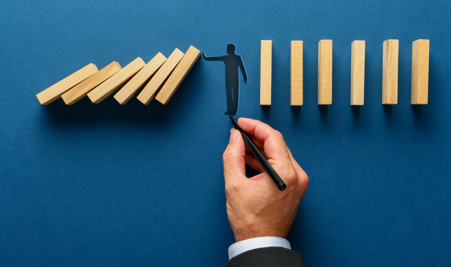 male hand drawing silhouette of a man making a stop gesture to prevent wooden dominos from collapsing. Over navy blue background