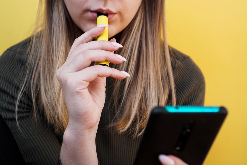 Lady smoking disposable vape infront of yellow background