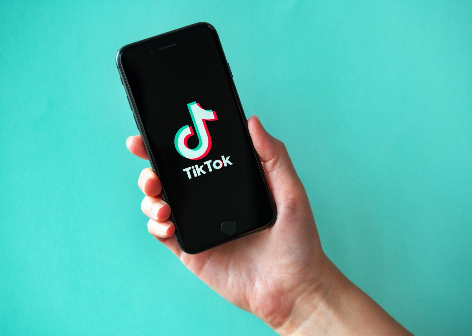 Studio shot of hand holding Apple iPhone 8 with TikTok logotype on a screen. Isolated on a vibrant cyan paper background