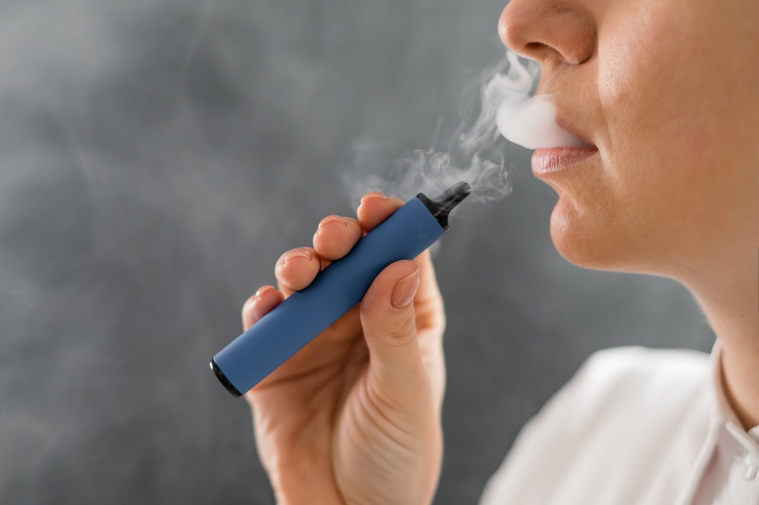 Caucasian woman smokes a blue disposable vape in the studio