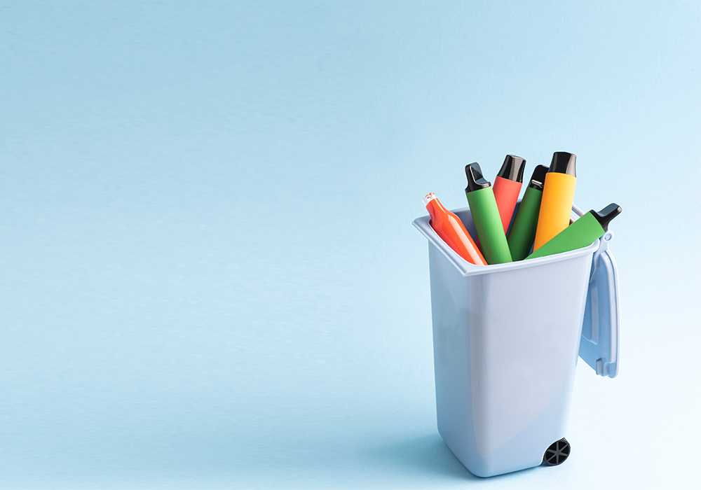 single use disposable vapes sticking out of a blue dustbin