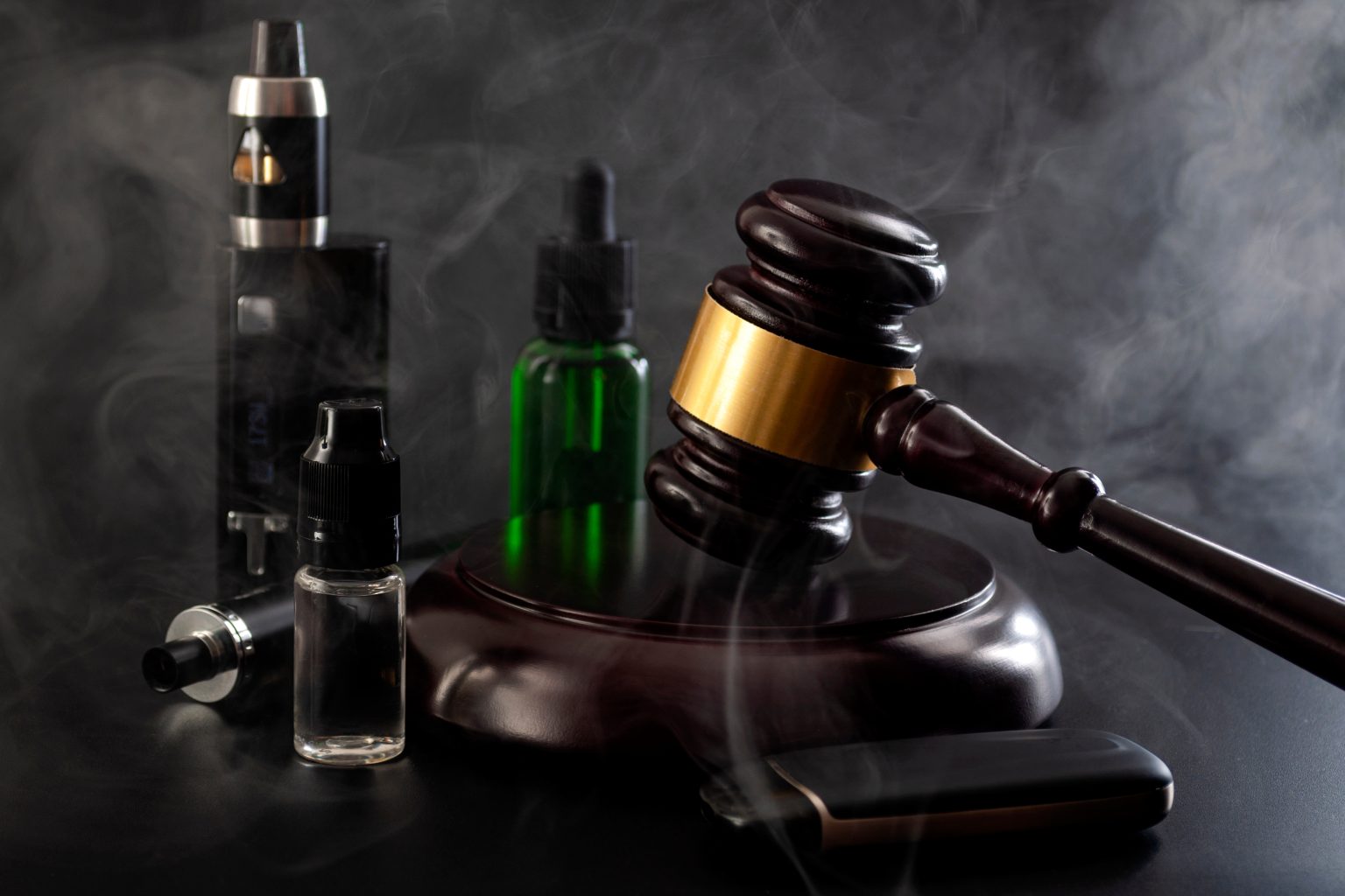 judge gavel, vape device, bottle of ejuice on black background