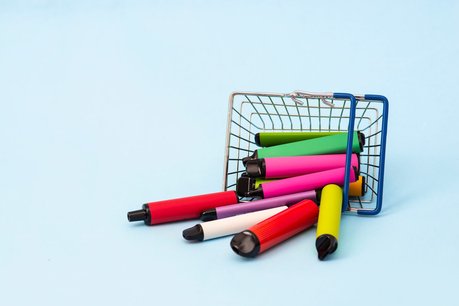 A set of multi-colored sticks - disposable vaping devices, electronic cigarettes in a shopping basket on a blue background