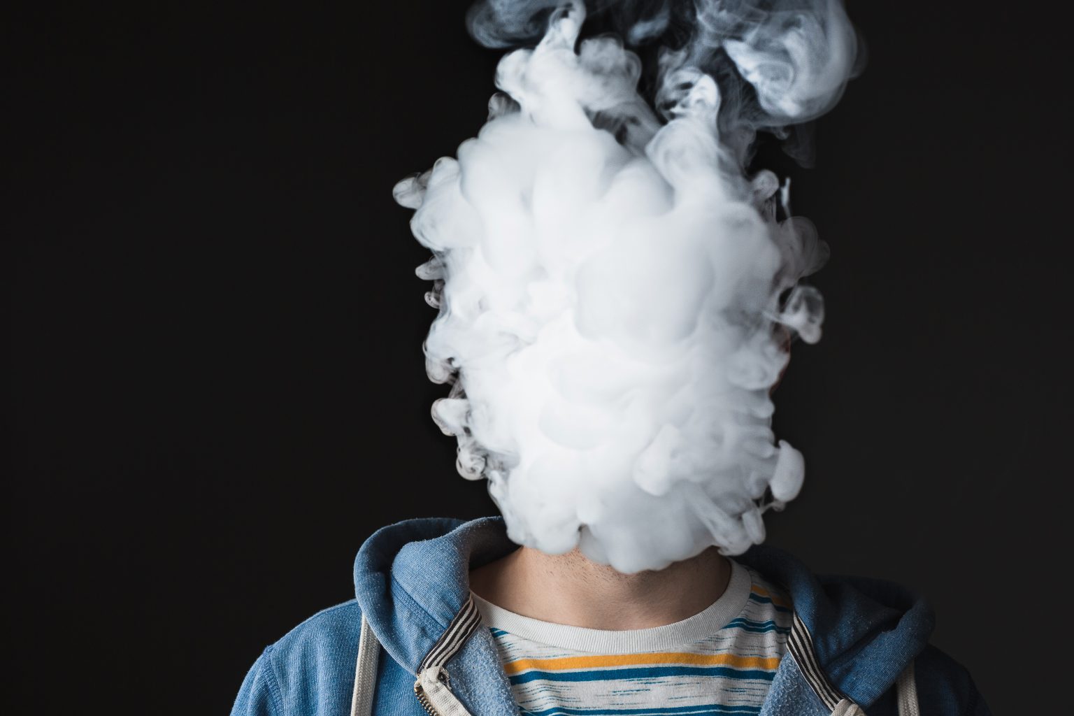 young man vaping on black studio background