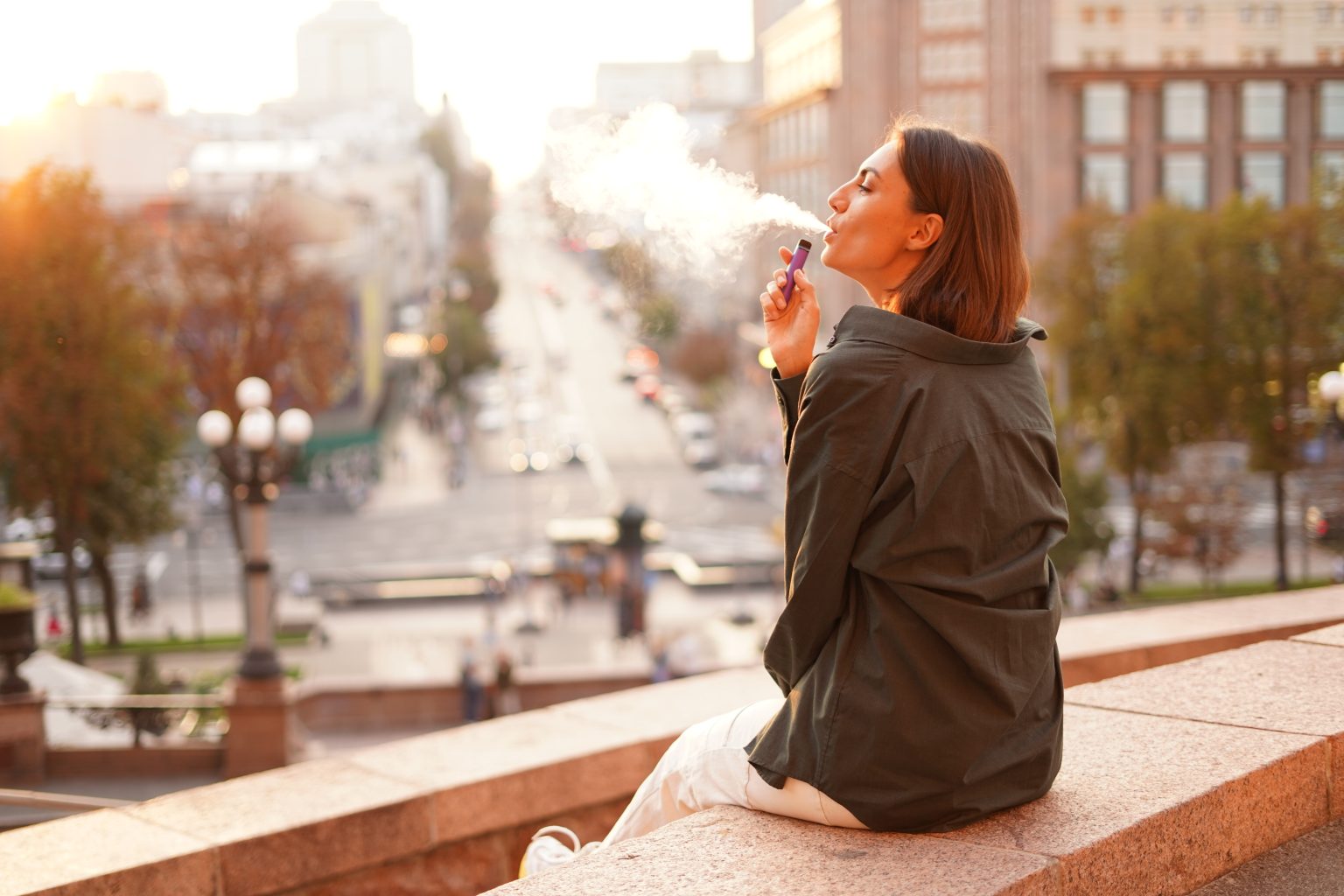 Woman at sunset with amazing city view, vaping electronic cigarette