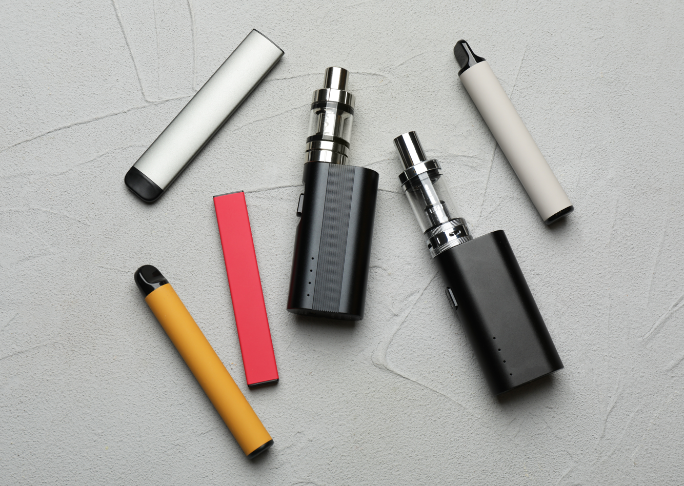 vape box mods, vape pen pod system and disposable single use vape devices all sat on a grey background