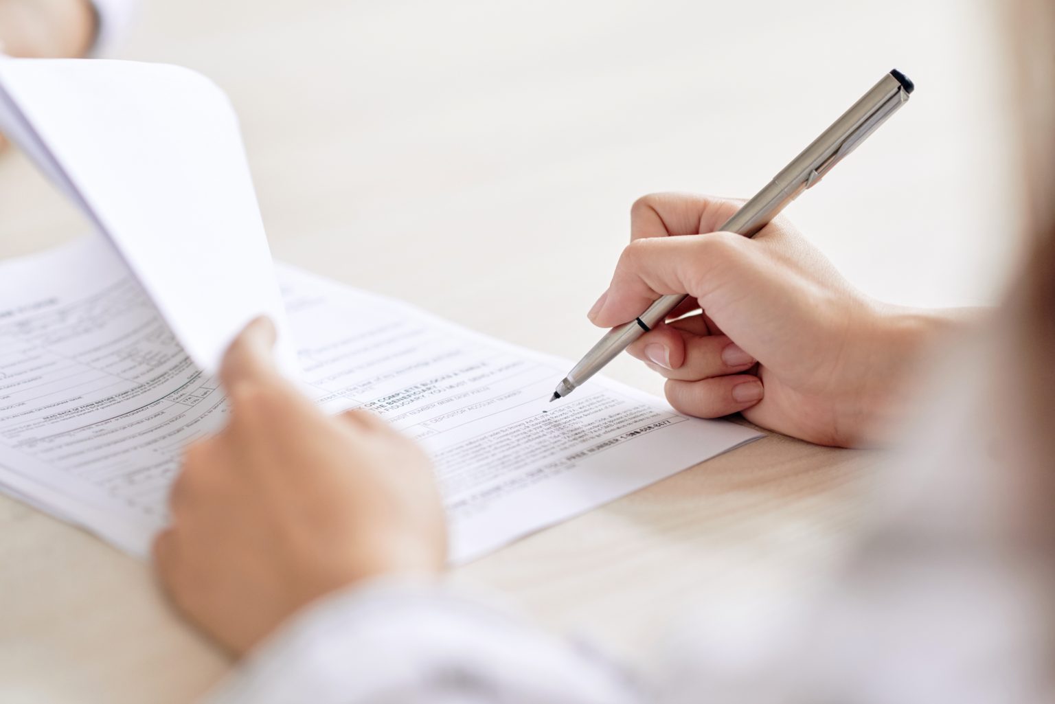 person with pen signing contract at desk in daylight